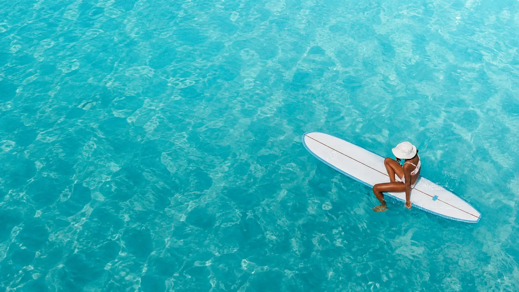 A surfer resting calmly and patiently on her board in still, clear water
